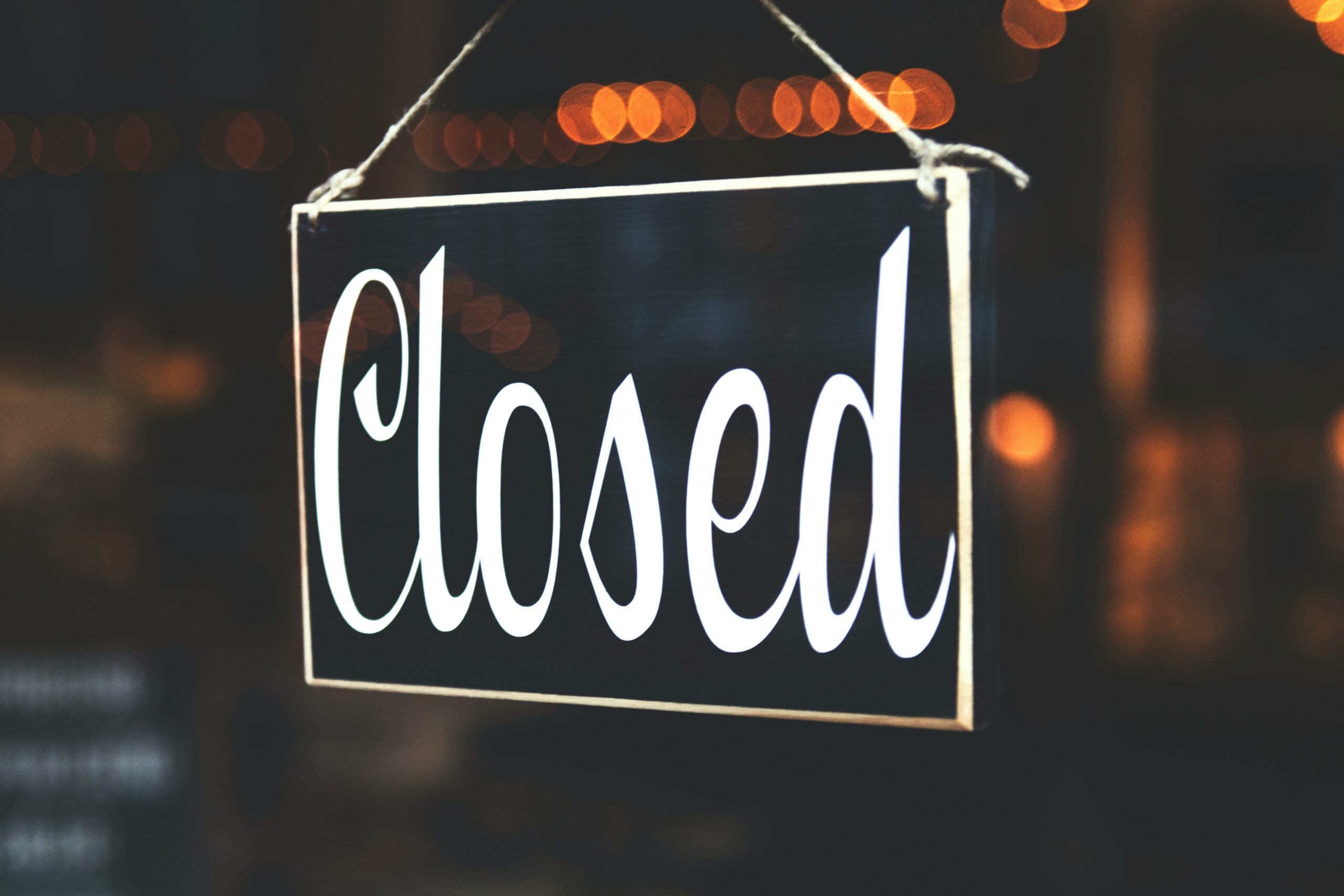 A close-up of a 'Closed' sign hanging against a blurred, bokeh background, creating a warm, inviting atmosphere.