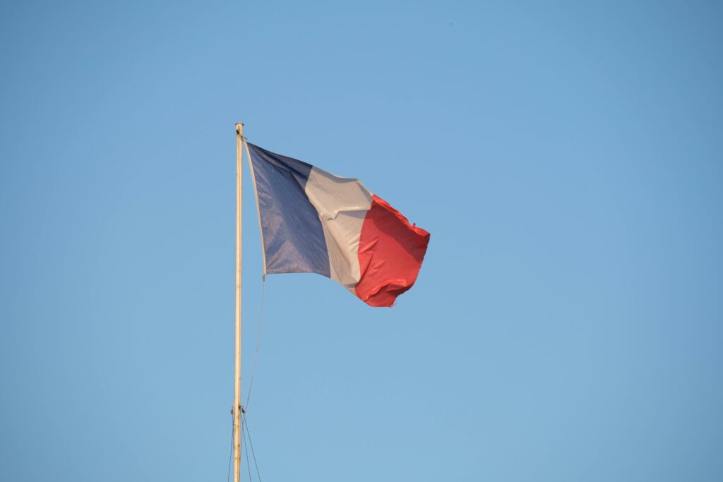 The French national flag waving on a flagpole against a clear blue sky.
